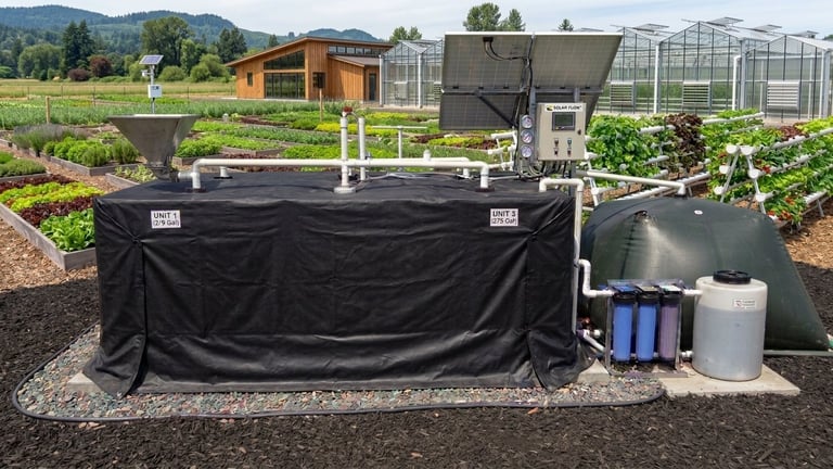 Aquaponics system with black tank and filtration equipment in farm setting with greenhouses and vegetable beds in background